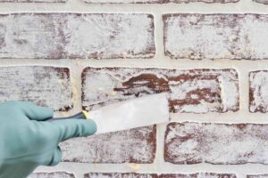 Close-up of applying gel stripper to painted brick fireplace with plastic wrap cover.