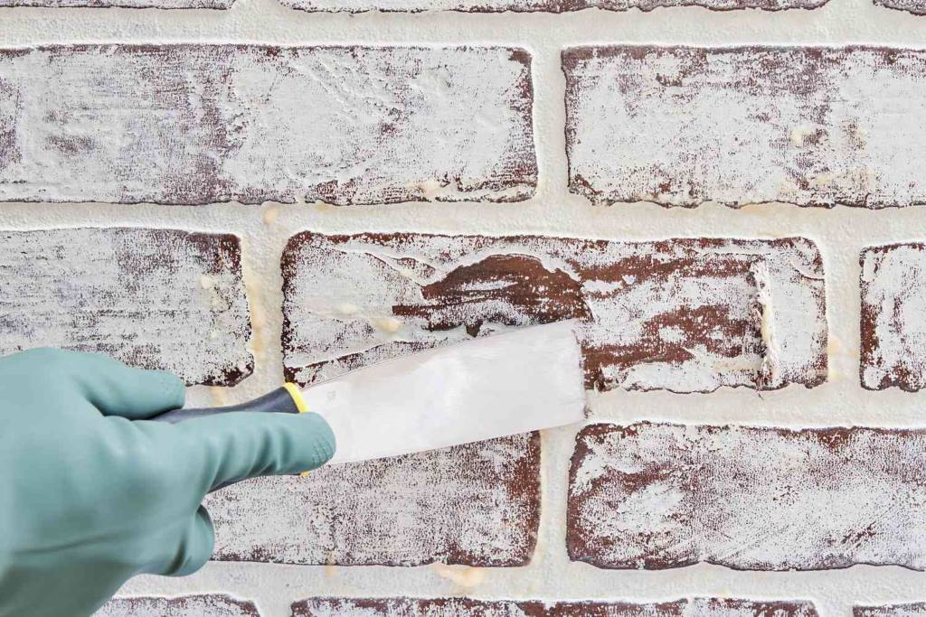 Close-up of applying gel stripper to painted brick fireplace with plastic wrap cover.
