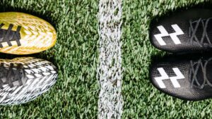 Close-up comparison of soccer cleats vs football cleats stud patterns on grass field